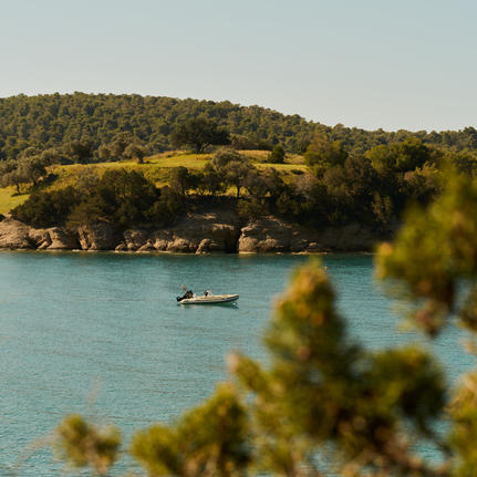 Turquoise waters and golden hillside at Amanzoe's beach club, with a moored boat visible offshore.