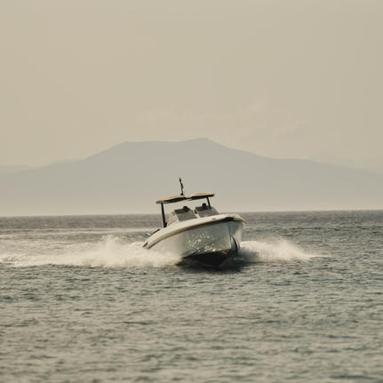 Wally One powerboat moored in calm waters off Amanzoe, with distant mountains visible under hazy skies.