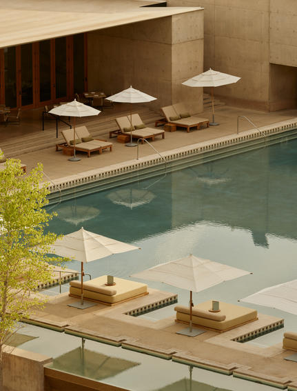 Amangiri's indoor plunge pool with pendant lighting, wooden loungers and cream umbrellas reflected in still water.