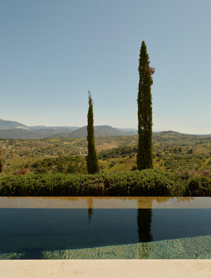 Pool pavilion at Amanzoe with cypress trees reflected in still water, Greek landscape beyond.