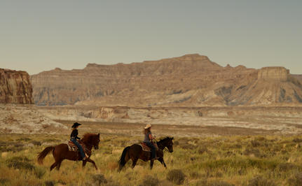 Two riders on horseback traversing the desert landscape at Amangiri, with red rock formations in the distance.