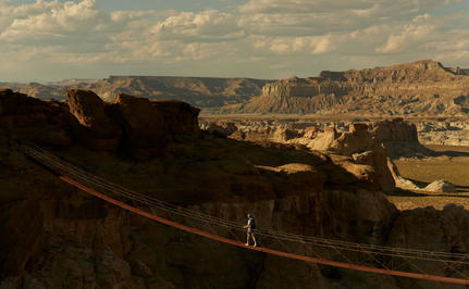 Climber traversing a via ferrata route across red rock formations at Amangiri, Utah.