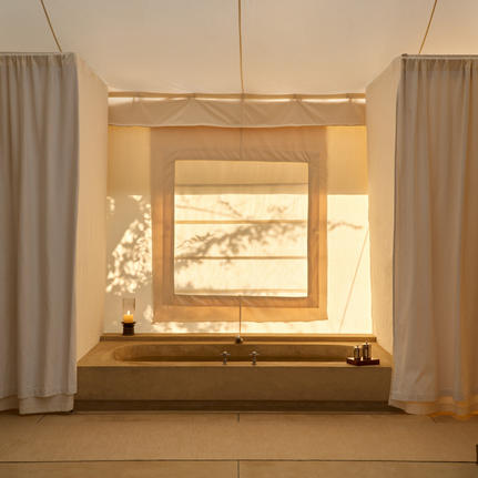 Bathtub set into wooden surround within tent bathroom at Aman-i-Khas, with framed artwork above and sheer curtains either side.