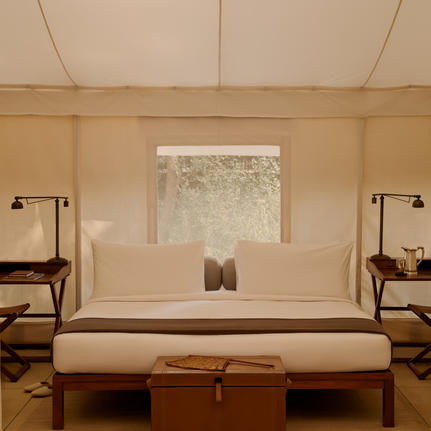 Tent bedroom at Aman-i-Khas with cream furnishings, symmetrical bedside tables and a central window overlooking Indian landscape.