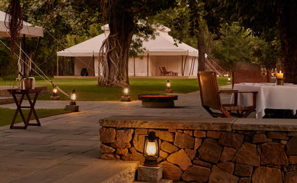 Tented pavilion at Aman-i-Khas illuminated at dusk, surrounded by trees and a stone firepit.