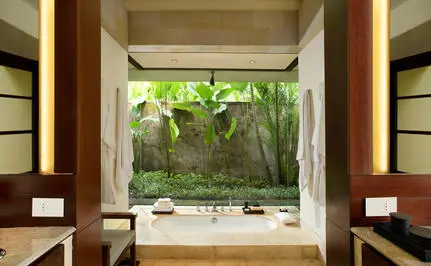 Bedroom at Aman Villas at Nusa Dua with garden view through open doors and tropical plants.