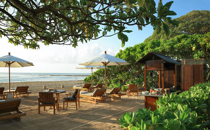 Beachfront terrace at Aman Villas at Nusa Dua with wooden loungers, tropical plants, and ocean views.