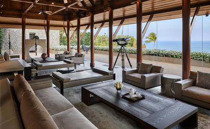 Amanpuri ocean villa lounge with wooden beams, ocean views, and contemporary furnishings overlooking the coastline.