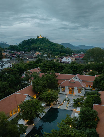 Amantaka residence with terracotta roof overlooking misty mountains and valley town at dusk.
