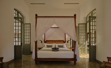 Amantaka Mekong Pool Suite principal bedroom with four-poster bed, symmetrical windows and neutral décor.