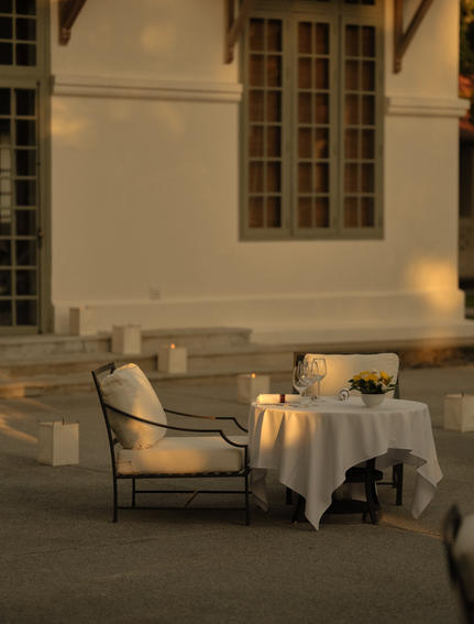 Candlelit poolside dining table at Amantaka, set for an intimate dinner beneath colonial architecture.