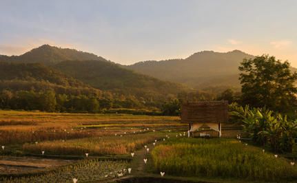 Intimate dinner setup in a rice paddy at Amantaka, with a candlelit table beneath a hut, mountains rising beyond.