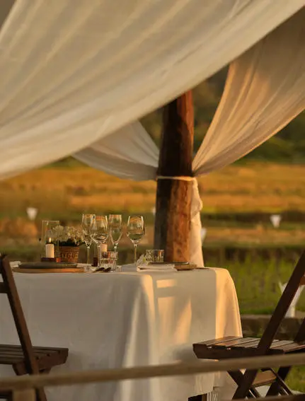 Intimate outdoor dining table set at Amantaka with draped fabric canopy and countryside views at dusk.