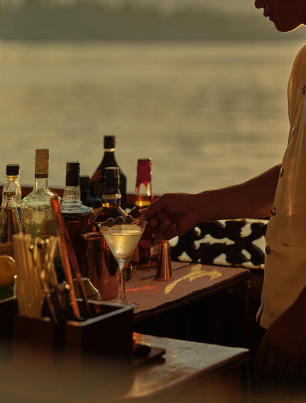 Cocktail-making session during a Mekong sunset cruise at Amantaka, with spirit bottles and mixing tools arranged on a wooden table.