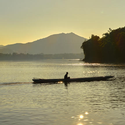 Local fisherman in traditional wooden boat on the Mekong River at sunset, Amantaka.