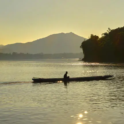 Local fisherman in traditional wooden boat on the Mekong River at sunset, Amantaka.