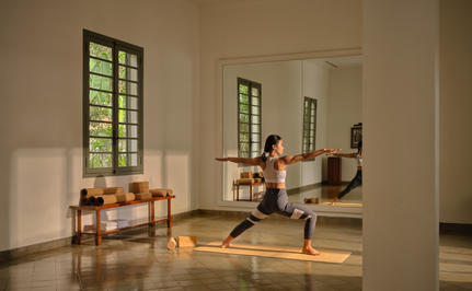 Yoga instructor leading a sunrise movement class at Amantaka, Laos, in a bright studio with wooden floors.