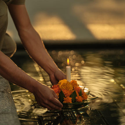 Hands releasing a lit flower krathong into water during Loy Krathong ceremony at Amantaka.