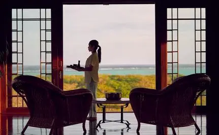Woman in yellow dress seated in spa relaxation area at Amanpulo, Philippines, overlooking tropical landscape.