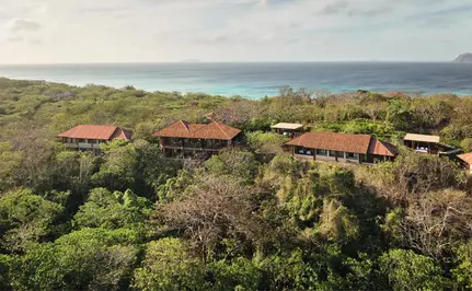 Amanpulo nestled among lush hillside vegetation with ocean views beyond.