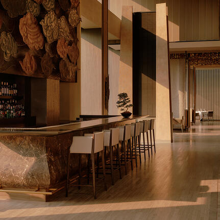 Bar at Aman Nai Lert Bangkok with wooden counter, stools, and warm ambient lighting.