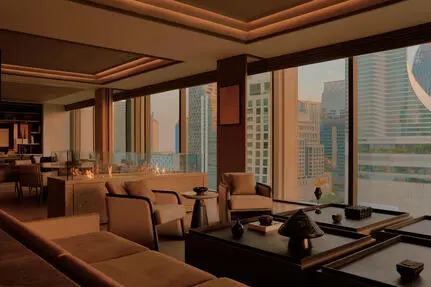 曼谷奈乐安缦酒店套房内，木质框架落地窗俯瞰城市景观，配有米色扶手椅和低调家具。