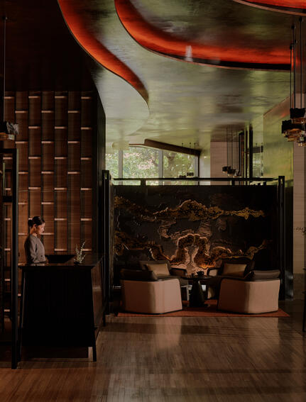 Aman Nai Lert Bangkok arrival lobby with warm lighting, brick walls, and sculptural elements.