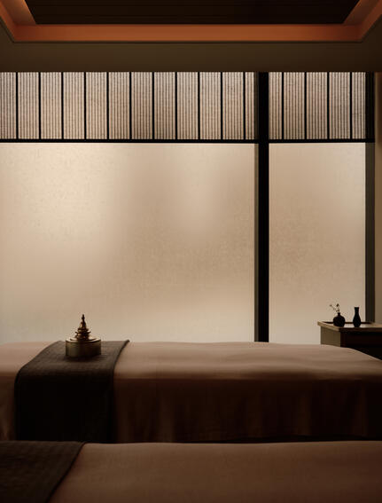 Spa treatment room at Aman Nai Lert Bangkok with sunlit window and minimalist wooden furnishings.