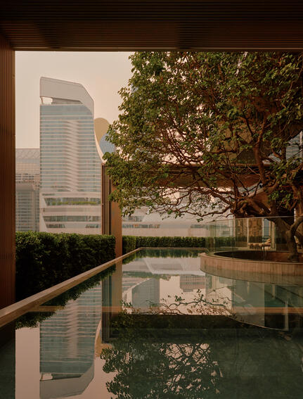 Swimming pool at Aman Nai Lert Bangkok with view of modern building and tree reflected in still water.