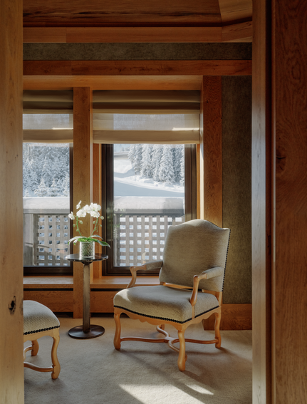 Wooden-framed reading nook at Aman Le Mélézin with upholstered chair overlooking snowy Alpine landscape.