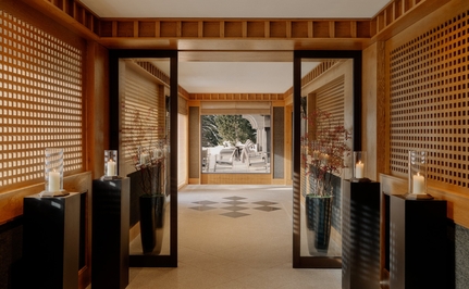 Stone entrance hall at Aman Le Mélézin with wooden walls and open doors framing snowy Alpine views.