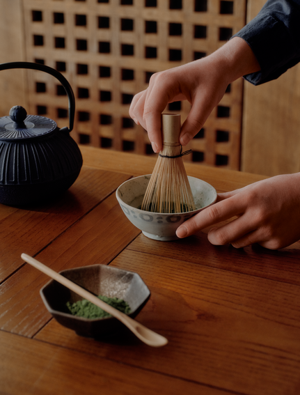 Hands preparing matcha tea at Aman Le Mélézin, whisking powder in a traditional bowl.