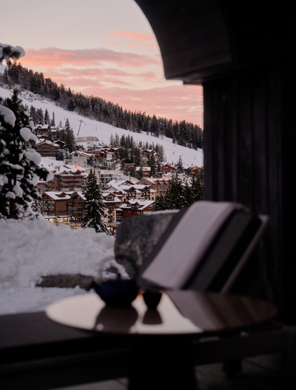 Sunlounger on a terrace at Aman Le Mélézin overlooking snow-covered Alpine slopes at dusk.