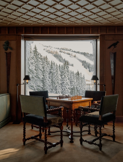Salon at Aman Le Mélézin with wooden chairs at a desk facing a window overlooking snowy Alpine forest.
