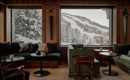 Interior of Aman Le Mélézin with wooden panelling, desks and large windows framing snowy mountain views.