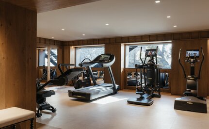 Gym at Aman Le Mélézin with exercise equipment and mountain views through windows.