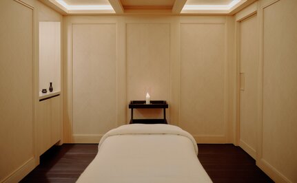 Spa wellness treatment room at Aman Le Mélézin with a massage bed, neutral panelled walls, and soft overhead lighting.