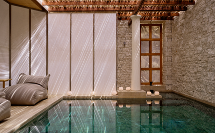 Piscina de bienestar cubierta con agua turquesa en el resort Amanzoe, Grecia, junto a zona de descanso con cojines.
