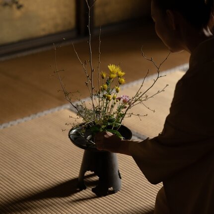 A hand arranging fresh flowers and branches in a dark vessel at Aman Kyoto.