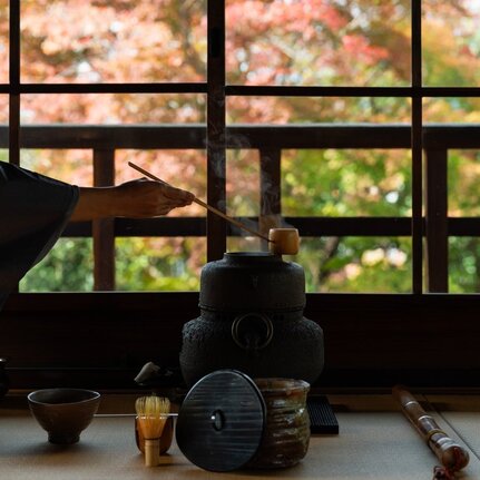 Silhouetted tea ceremony utensils arranged on a low table at Aman Kyoto, with garden views beyond latticed windows.