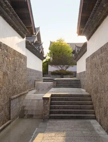 Stone pathway with steps leading to a courtyard at Amandayan, China, framed by modern architectural walls.