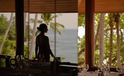 Silhouetted figure standing on a wooden terrace at Amanpuri, Thailand, overlooking tropical landscape at dusk.