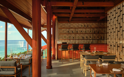 Amanpuri's Nama dining venue with wooden beams, sake bar seating, and ocean views through large windows.