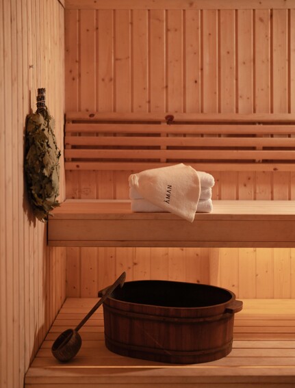 アマンプリのスパ施設内にある木製サウナ小屋。木製のベンチに白いタオルと瓶が置かれ、床には黒い桶とひしゃくがある。