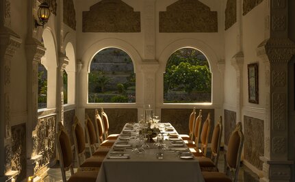 Royal dinner setup at Amankila, Karangasem, with candlelit table beneath arched pavilion overlooking gardens.