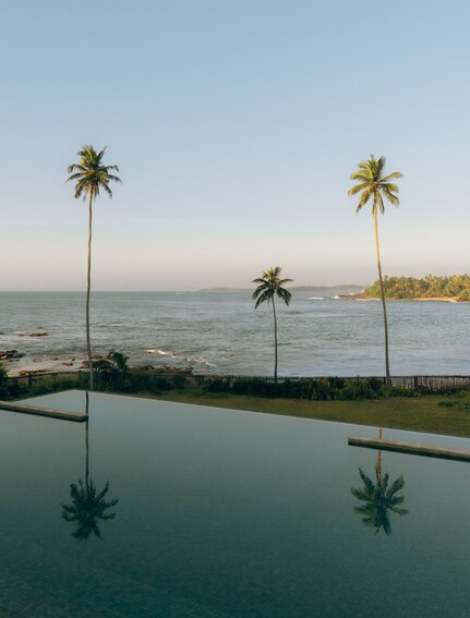 Infinity pool overlooking the Indian Ocean at Amanwella, Sri Lanka, with palm trees reflected in still water.
