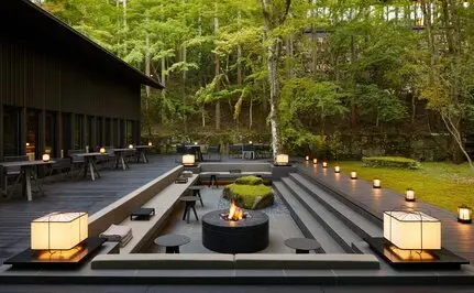 Pabellón iluminado al atardecer en Aman Kyoto, con linternas y fuego central reflejados en el agua.