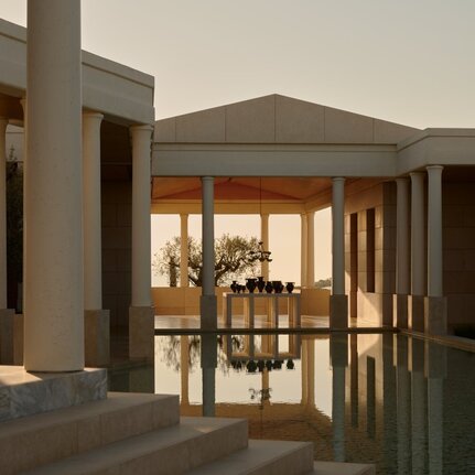 Amanzoe resort entrance at dusk, featuring illuminated wooden doors and columns framing the doorway.