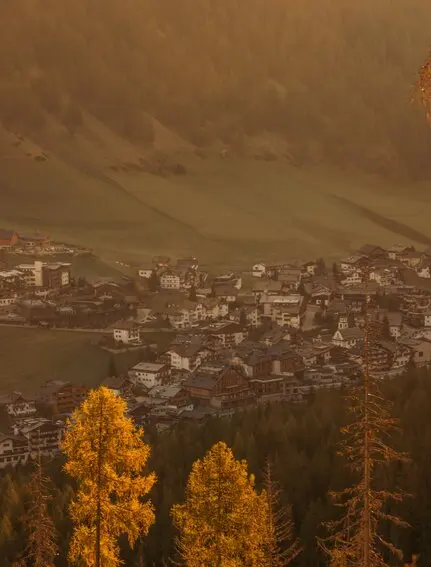 Veduta autunnale della valle di San Cassiano dal resort Aman Rosa Alpina, con larici dorati in primo piano.