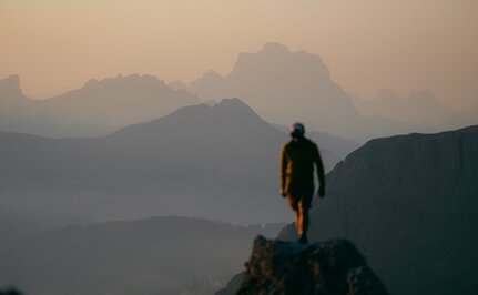 Hiker stood on mountain ridge at sunrise, Aman Rosa Alpina resort, layered peaks in mist below.